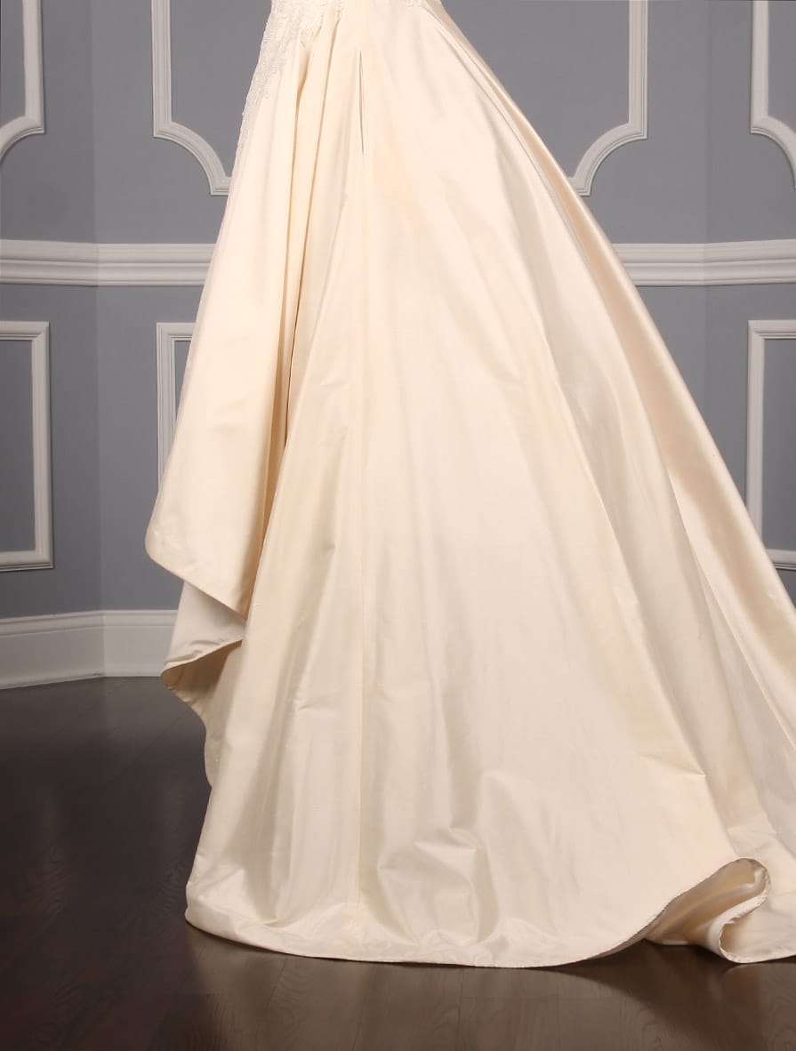 This Romona Keveza Legends L7130 wedding dress is Brand New!  It is made from beautiful silk shantung taffeta with lace appliques.  The ivory color is a vanilla shade, a bit of a warmer ivory.  This Romona Keveza Legends wedding dress is strapless with a ballgown silhouette, a high low hemline and a chapel train.  Side seam pockets are hidden in the skirt and are perfect for holding a few tissues or your lipstick.  You will definitely 'wow' your guests as you walk down the aisle in this stunning couture creation!